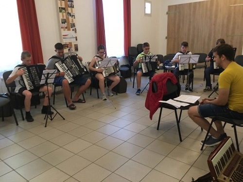 Fiatalok harmonikáznak kottaállványok előtt a táborban.