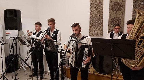 Fiatal zenészek trombitával, harmonikával és tubával játszanak kottaállványok mögött.