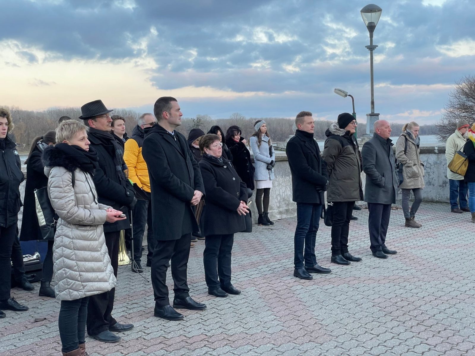 Ünneplő közönség áll a szabadban a folyóparti megemlékezésen.