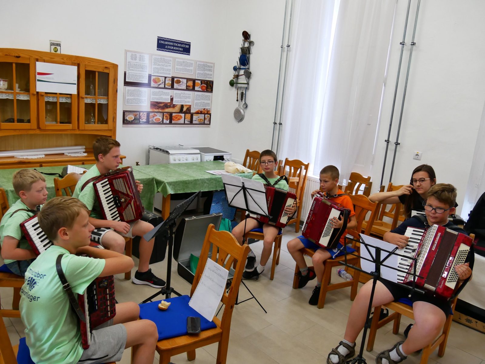 Gyerekek harmonikáznak egy teremben, kottaállványok előtt.