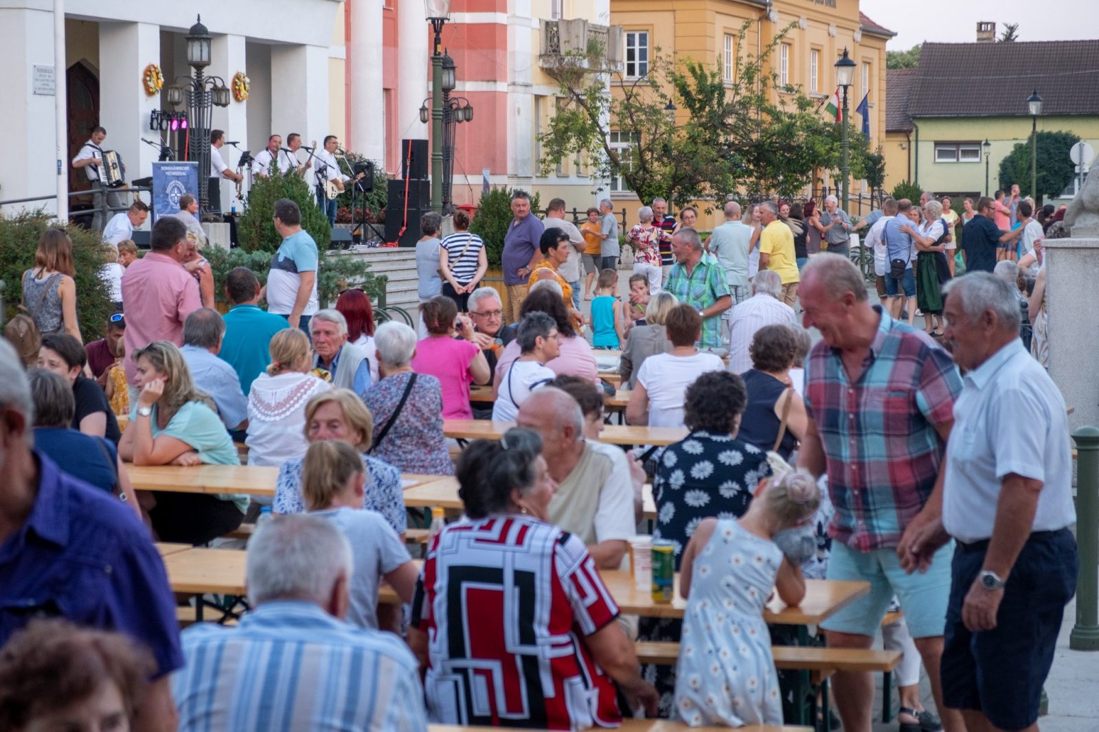 Zöld pólós gyerekek harmonikákkal csoportképen a faszerkezetes pavilon alatt.