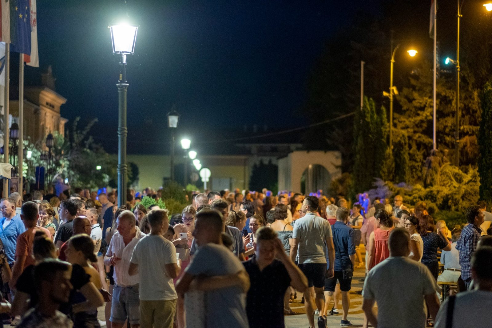 Táncoló és beszélgető tömeg az esti utcabálon, lámpafényben.
