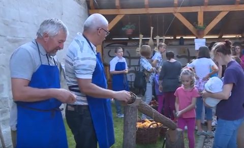 Kék kötényes férfiak kemencénél sütnek, mellettük sorban álló vendégek.
