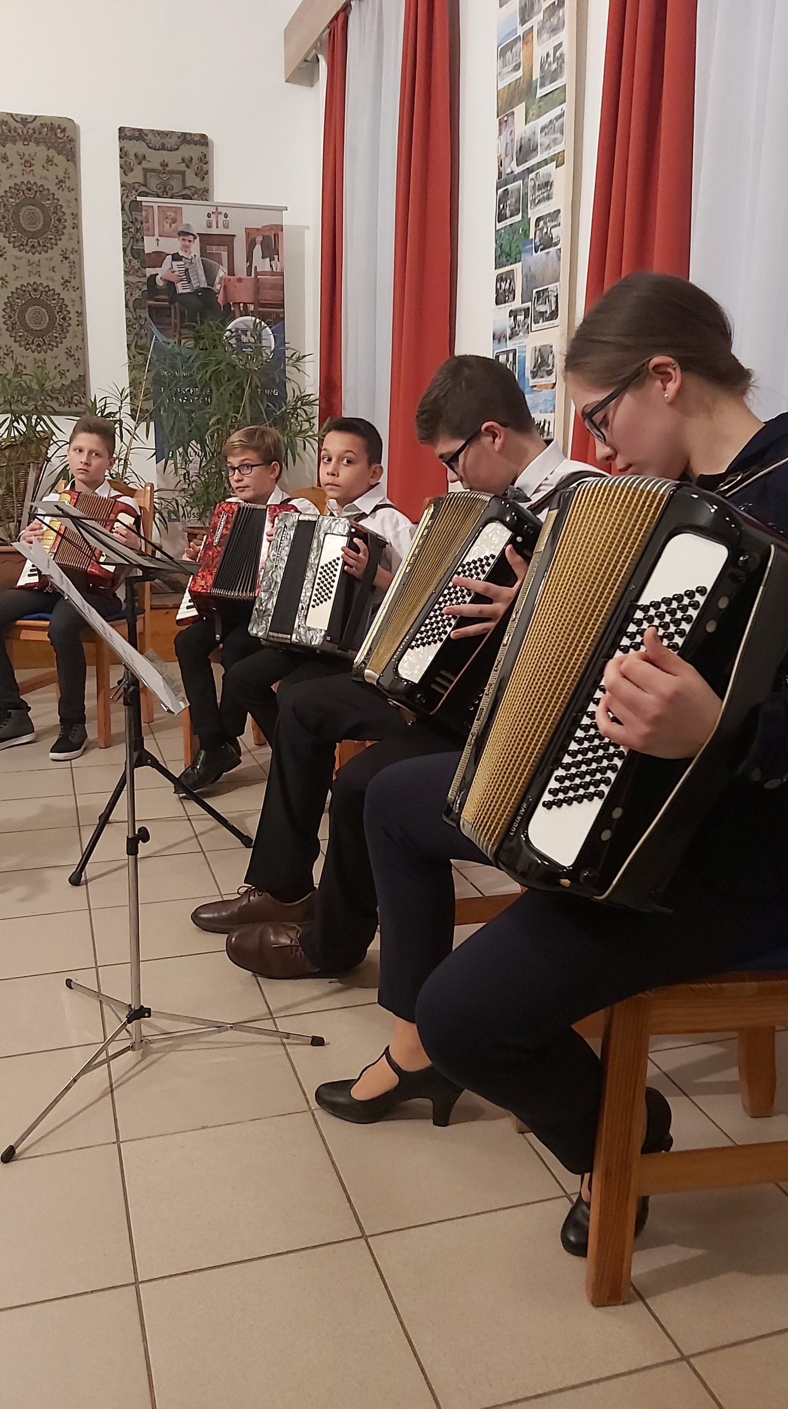 Fiatalok harmonikáznak kottaállvány mögött egy teremben.