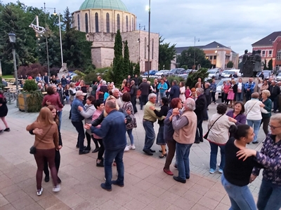 Táncoló vendégek és zenekar egy teremben, hárfával és harmonikával.