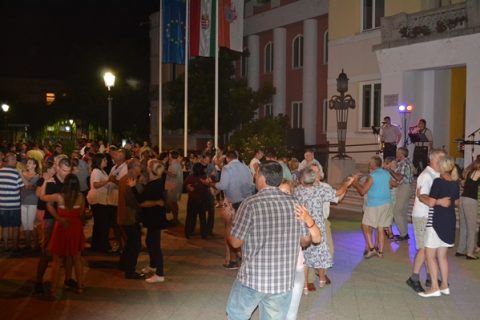 Táncoló tömeg az esti utcabálon, a háttérben világító épületek.