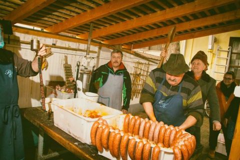 Frissen töltött kolbász tálcán, mögötte a disznótoros résztvevői.