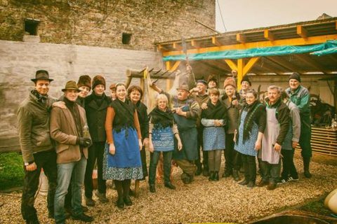 Große Gruppe in Mänteln und Schürzen beim Gruppenfoto im überdachten Hof.