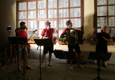 Zenekar harmonikával és mikrofonokkal lép fel egy teremben.