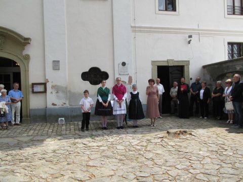 Népviseletbe öltözött asszonyok és lányok sorban állnak a templom fala mellett.