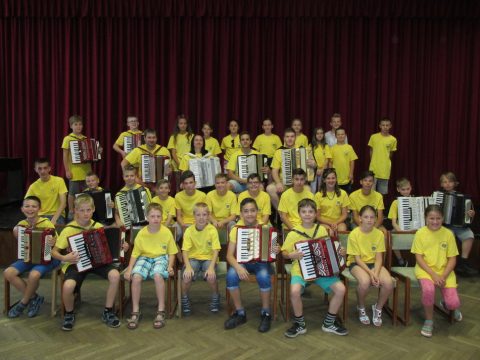 Gruppe von Kindern in gelben T-Shirts mit Akkordeons auf der Bühne.