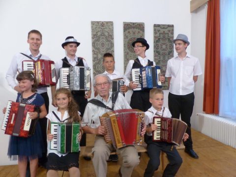 Fiatalok népviseletben, harmonikákkal egy teremben.