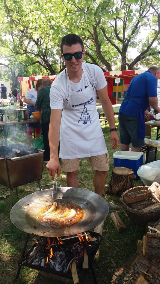 Férfi nagy serpenyőben süt nyílt tűzön egy vásárban.