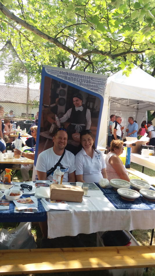 Sátor alatt terített asztalok és vendégek egy szabadtéri rendezvényen.