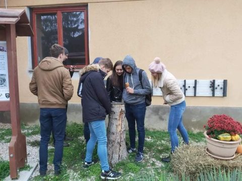 Fiatalok összehajolva néznek valamit egy épület fala előtt.
