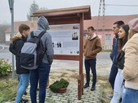 Fiatalok kabátban egy kültéri információs tábla előtt, ködös őszi reggelen.