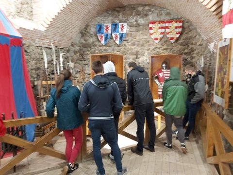 Látogatók egy boltíves kiállítótérben, a falon címeres zászlókkal.