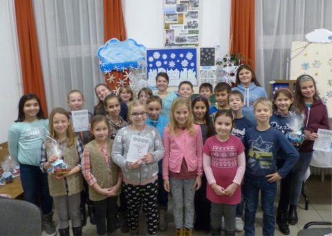 Gyerekek csoportképe egy tanteremben, télies dekoráció előtt.