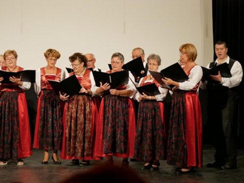 Női kórus népviseletben énekel kottából, mellettük férfi énekes.