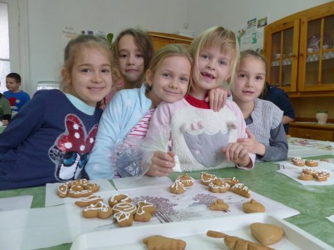 Öt gyerek mosolyog a mézeskalácsokkal teli asztal fölött.