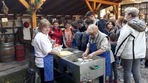 Asszonyok sütnek egy fedett szín alatt, előttük sorban álló gyerekek.